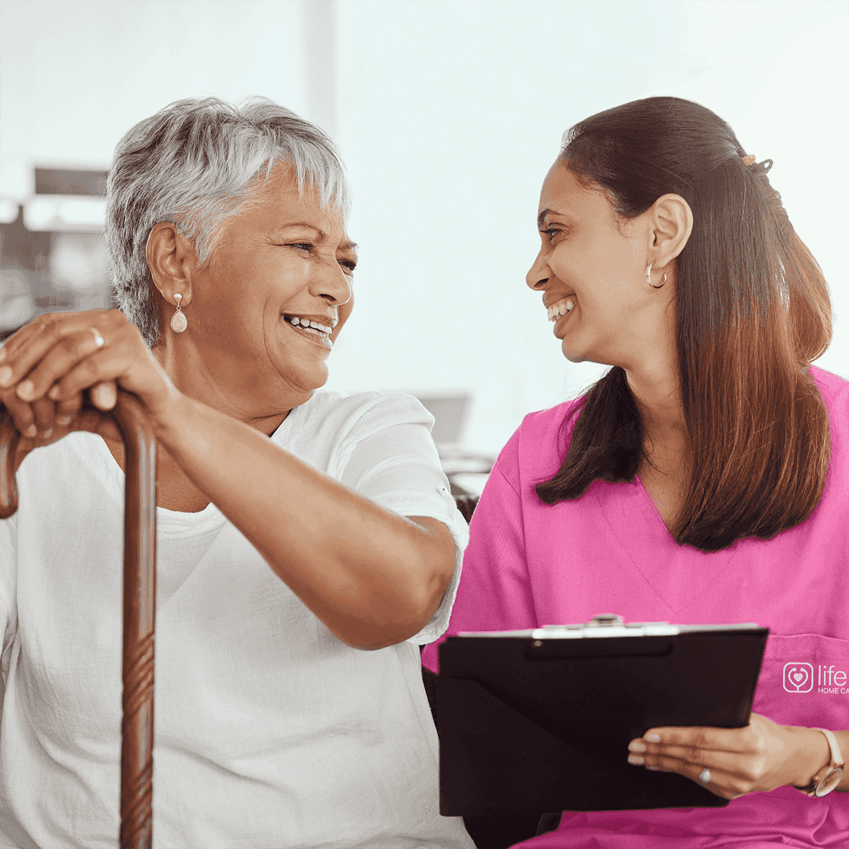 caregiver and elderly woman sitting on couch smiling