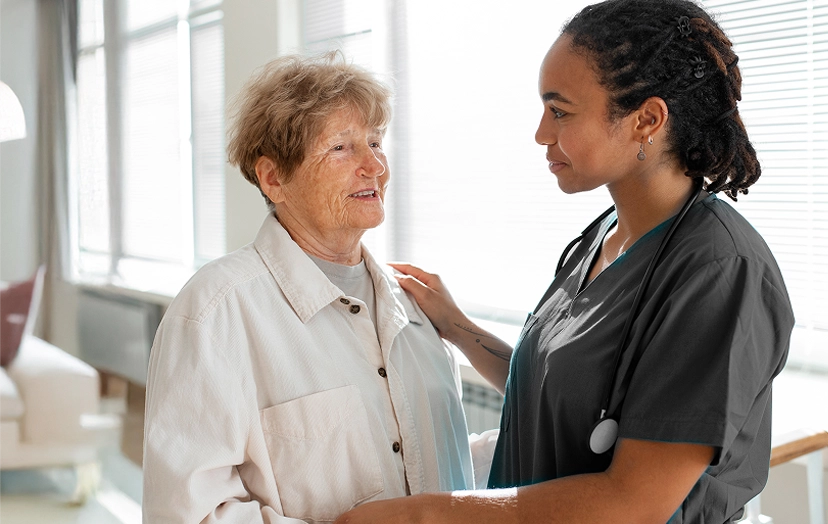 Nurse comforting elderly woman at home during palliative care visit