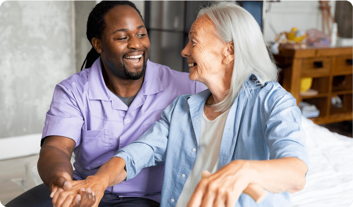 A healthcare professional laughing and sharing a friendly moment with an elderly female patient inside a residential setting.