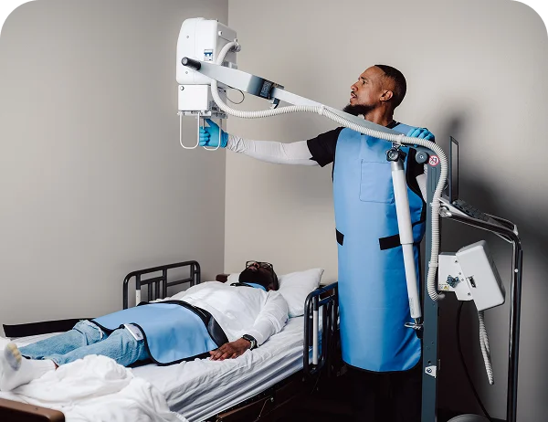 Male technician using portable X-ray equipment to perform diagnostic imaging on a patient lying in bed at home.