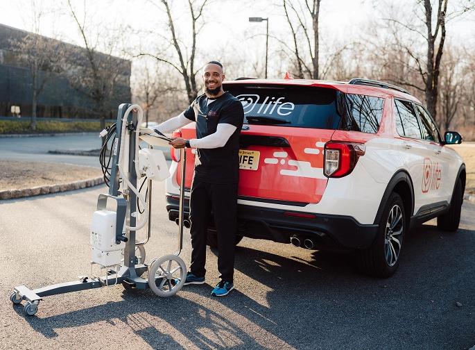 MobileCare technician with portable X-ray machine standing next to branded vehicle, providing in-home imaging services.